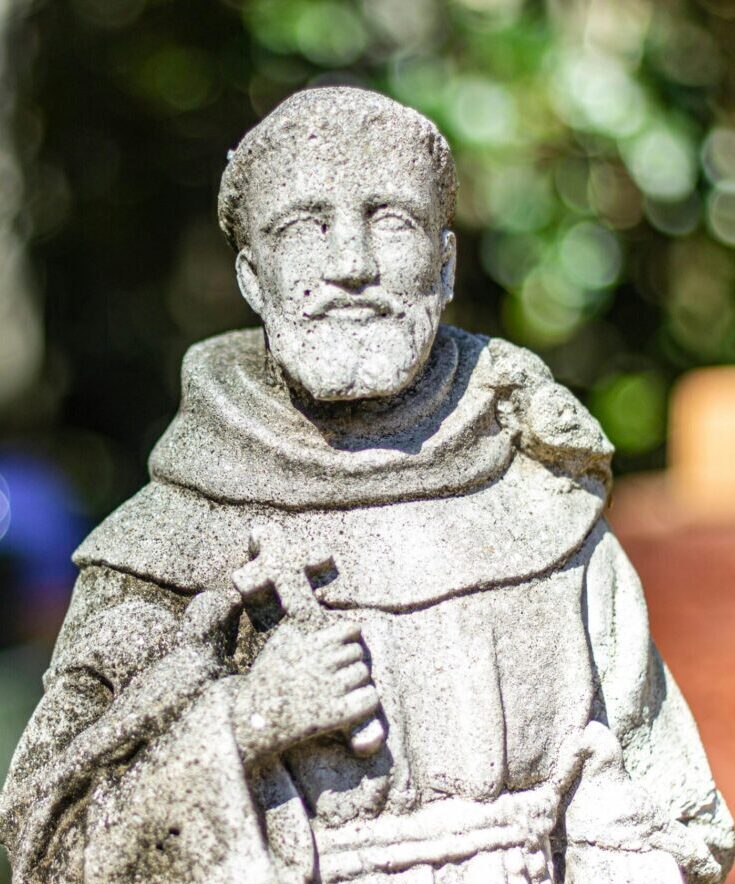 A serene stone statue of Saint Francis holding a cross in Gainesville, Florida.